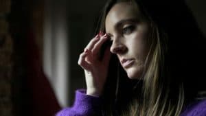 Woman with hand on forehead looking out window