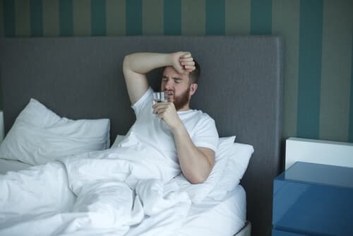 man in bed sipping water with hangover